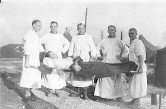 Staged photo illustrating 5 Officers with a patient on a litter, pertaining to the 164th General Hospital while stationed near La-Haye-du-Puits, France. 1st Lieutenant William E. Sheffield is the person in the middle. Picture courtesy Robert Sheffield