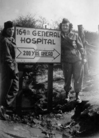 Sign designating the 164th General Hospital, La Haye-du-Puits, France. Picture taken 4 Jun 45.  Standing from L to R: 2d Lt. Dorothy F. Levitsky, N-762231 and 2d Lt. Agnes C. Stern, N-762236.