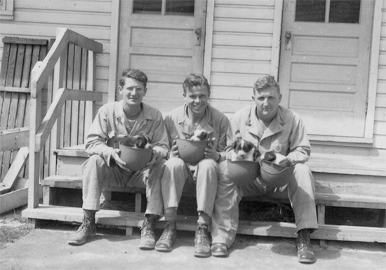 Members of the 48th Field Hospital take a break in front of one the Enlisted Men's barracks. They hold 4 new-born puppies in their liners. 