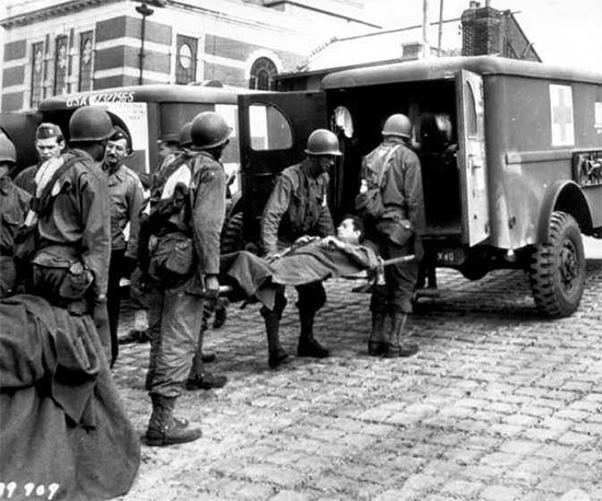 Following arrival by ship from France, a patient is transferred to a 3/4-ton ambulance waiting at the docks to take him to a hospital in England. Photograph taken 12 June 1944.