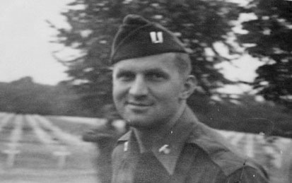 Captain Robert M. Farrell, Commanding Officer, 603d Quartermaster Graves Registration Company, with a partial view of the H-C Cemetery in the background.